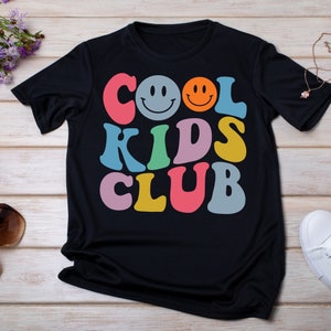 May include: Black t-shirt with a colorful graphic that says "COOL KIDS CLUB" with two smiley faces.