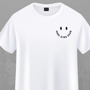 May include: White t-shirt with a black graphic of a smiley face and the text "COOL KIDS CLUB" around the face.