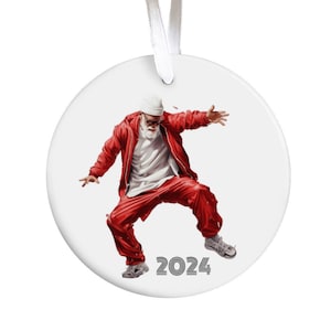 May include: A round white Christmas ornament featuring a dancing Santa Claus in a red tracksuit, white hat, and glasses. The year "2024" is printed in black at the bottom. A white ribbon is attached for hanging.