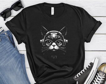 May include: Black t-shirt featuring a black and white illustration of a cat wearing headphones. The cat has large eyes and a detailed design. The shirt is paired with blue jeans, black sunglasses, and black and white sneakers.