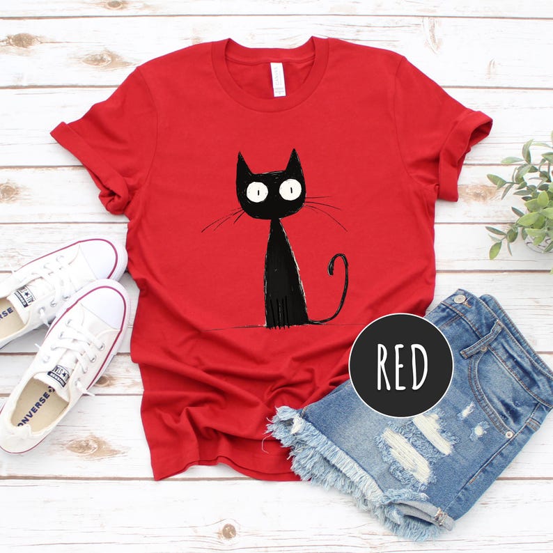 May include: Red t-shirt with a black cat illustration. The cat has large eyes and a long tail. The word "RED" is written in white on a black circle.