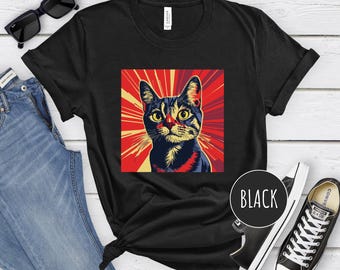 May include: Black t-shirt with a graphic of a cat in a pop art style with red, yellow, and blue colors. The text "BLACK" is printed on the shirt.