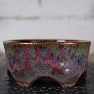 Peut inclure: Un pot de bonsaï en céramique avec un glaçage unique. Le pot a un design bas et large avec trois pieds. Le glaçage présente un mélange de couleurs, dont le violet, le rose, le vert et le marron, créant un aspect texturé. Idéal pour les petites plantes.