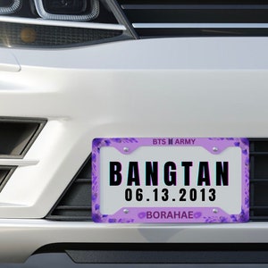 Puede incluir: Un coche blanco con un marco de matrícula morado y blanco que dice "BTS M ARMY" y "BANGTAN 06.13.2013 BORAHAE".
