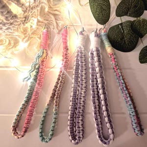 May include: Five colourful crocheted keychains with different patterns. The keychains are made with a variety of colours, including pink, blue, purple, and white.