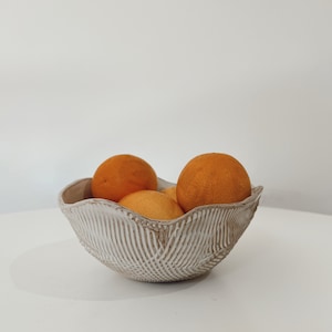 Puede incluir: Un tazón de cerámica blanco con una superficie texturizada, lleno de cuatro naranjas.