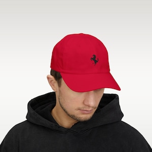 May include: A red baseball cap with a black horse logo on the front. The cap is made of a soft material and has a curved brim. The hat is a solid color and is a classic style.