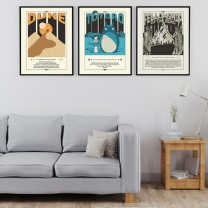 Może przedstawiać: Trzy oprawione plakaty filmowe wiszą na białej ścianie nad szarą sofą. Plakaty przedstawiają projekty w stylu vintage dla "Dune", "Totoro" i "Fellowship of the Ring". Każdy plakat ma czarną ramę i zawiera tekst i ilustracje.