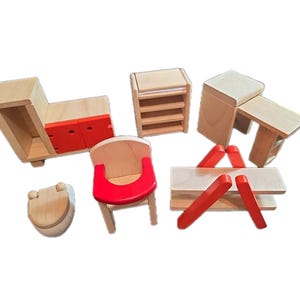 Op de afbeelding: Een set miniatuur poppenhuismeubels van hout, bestaande uit een kast met rode deuren, een kleine kast, een bureau, een toilet, een kinderstoel met een rode zitting en een picknicktafel met rode poten, gemaakt van lichtgekleurd natuurhout.