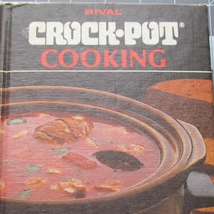 May include: A brown cookbook with the title "Rival Crock-Pot Cooking" on the front cover. The cover features a close-up of a brown Crock-Pot slow cooker filled with a red stew. The text "More than 300 recipes especially for the original Crock-Pot slow cooker" is printed on the bottom of the cover.