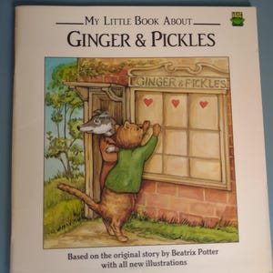 May include: A softcover book titled My Little Book About Ginger & Pickles, featuring an illustration of a cat and a dog looking into a shop window with three red hearts on the glass. The cover includes the LeapFrog logo and text credits.