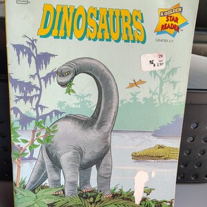 May include: A vintage children's book titled "DINOSAURS" with a large gray Brachiosaurus eating leaves. The cover features a green and blue background with a crocodile and a pterodactyl. The book is part of the Golden Star Reader series.