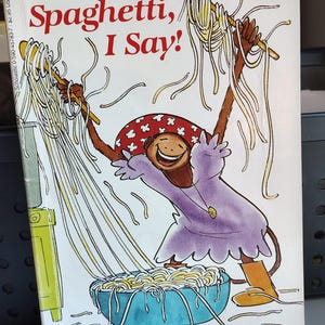May include: A children's book cover titled "More Spaghetti, I Say!" features a cartoon monkey character in a purple dress, holding spaghetti with wooden sticks. The book is part of the "Hello Reader!" series, level 2, for Kindergarten-Grade 2.