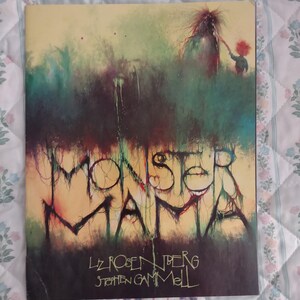 May include: A book cover titled Monster Mama by Liz Rosenberg and illustrated by Stephen Gammell. The artwork features a dark, abstract, and textured green and brown background with a small red-haired figure reaching toward a tall creature.