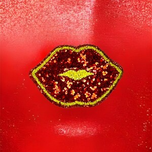 May include: A red glitter lip patch with a yellow outline. The patch is on a red background.