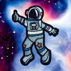 May include: A blue and white astronaut with a pink and blue striped suit and a black helmet with a white visor, giving a thumbs up, against a purple and blue galaxy background.