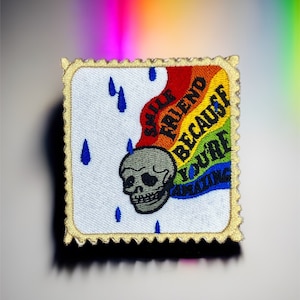 May include: A white embroidered patch with a rainbow, a skull, and the text "Smile Friend Because You're Amazing".