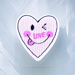 Puede incluir: Parche bordado en forma de corazón rosa con una cara sonriente guiñando un ojo, una lengua que sobresale y la palabra "LOVE" escrita en su interior.