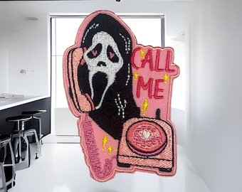 May include: Pink embroidered iron-on patch featuring a ghost wearing a white mask holding a pink phone with the text "CALL ME" in red and yellow stars.