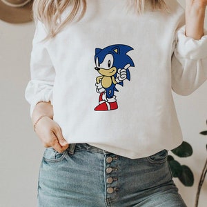 May include: White sweatshirt with a blue and yellow cartoon character wearing red shoes. The character is giving a thumbs up. The sweatshirt is being worn by a person with long blonde hair.