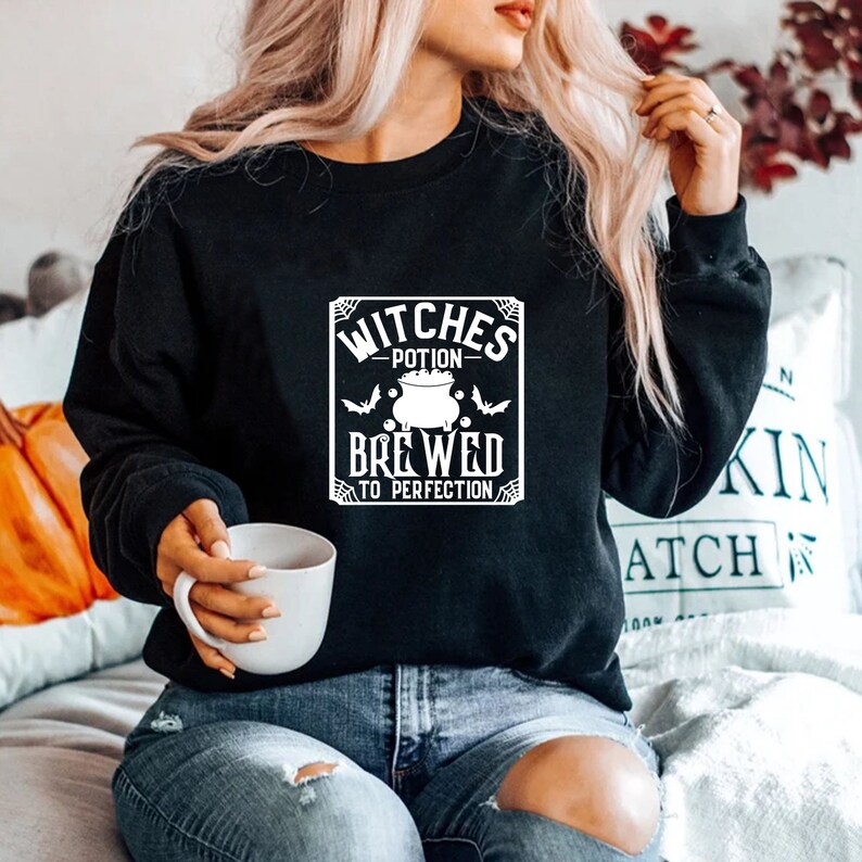 May include: Black sweatshirt with a white graphic design that says "Witches Potion Brewed to Perfection" with a cauldron and bats.