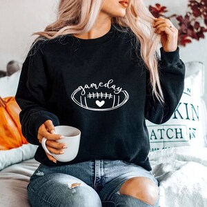 May include: Black sweatshirt with a white graphic of a football with the word "gameday" written on it.