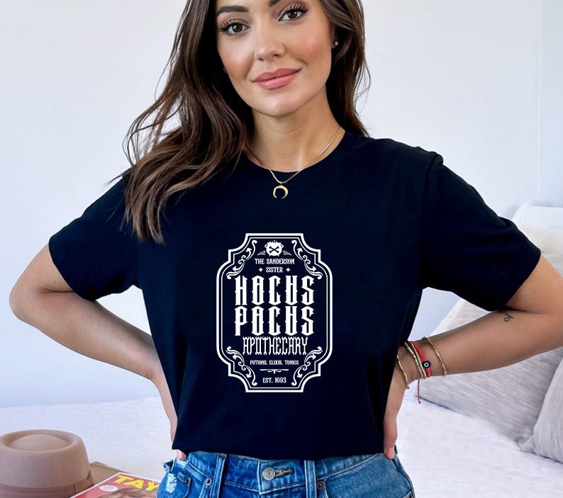 May include: A black t-shirt featuring a white graphic of a vintage label that reads "The Sanderson Sister + Hocus Pocus Apothecary, Potion Elixir Things, Est. 1933."
