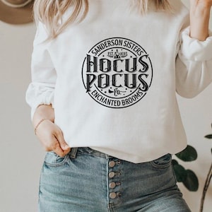 May include: White sweatshirt with a black circle graphic that says "Sanderson Sisters Est. 1693 Hocus Pocus Co. Enchanted Brooms"