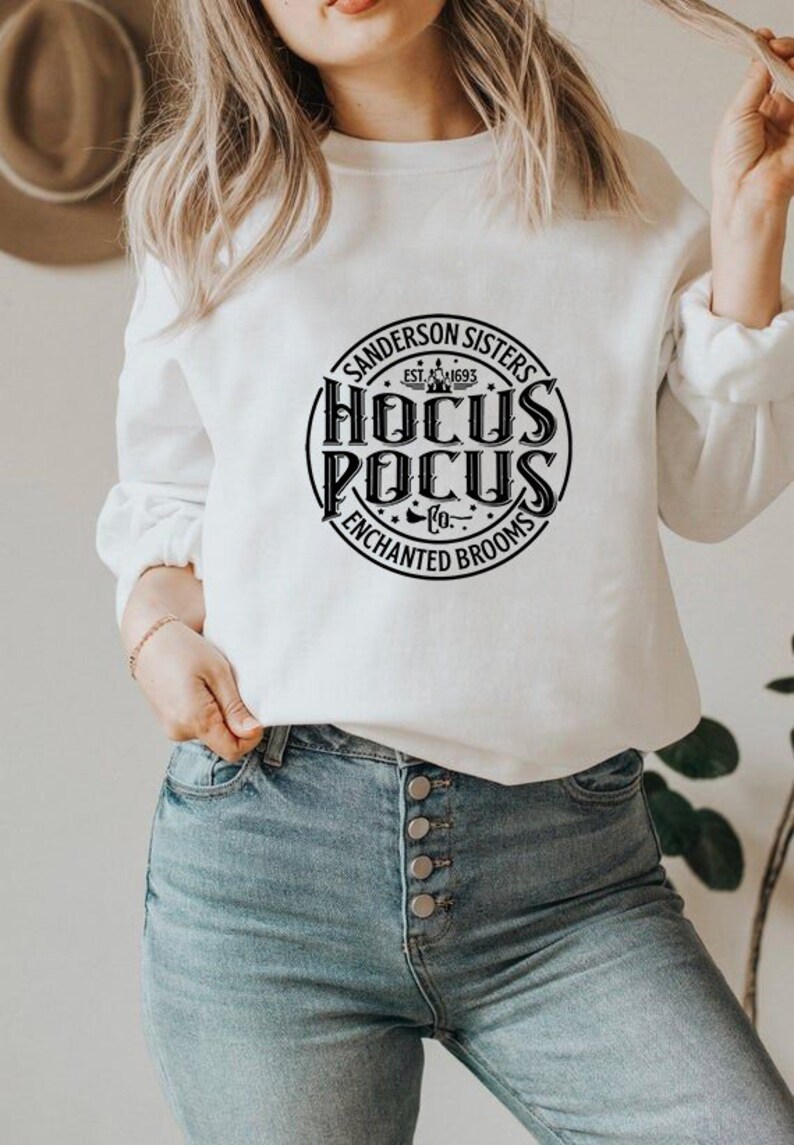 May include: White sweatshirt with a black circle graphic that says "Sanderson Sisters Est. 1693 Hocus Pocus Co. Enchanted Brooms"