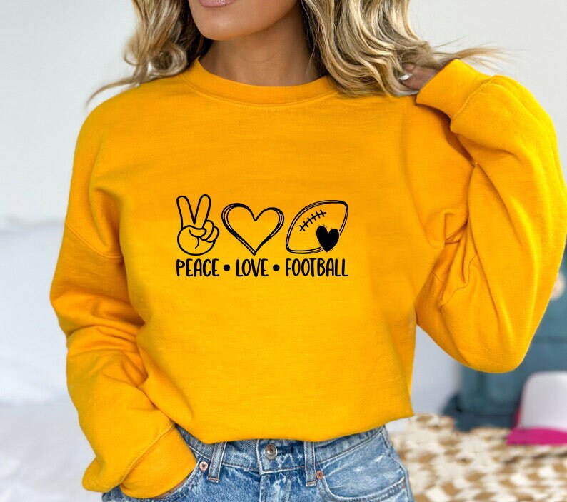 May include: Yellow sweatshirt with a peace sign, heart, and football graphic. The text reads "Peace Love Football".