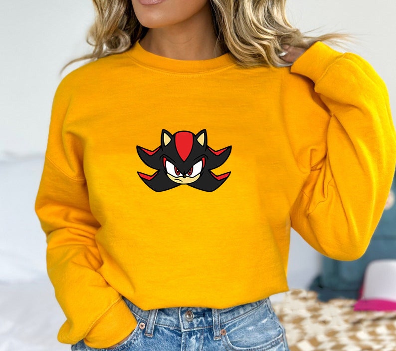 May include: A yellow sweatshirt with a black and red cartoon character on the front. The character has red eyes and a black and red spiky design around its head.
