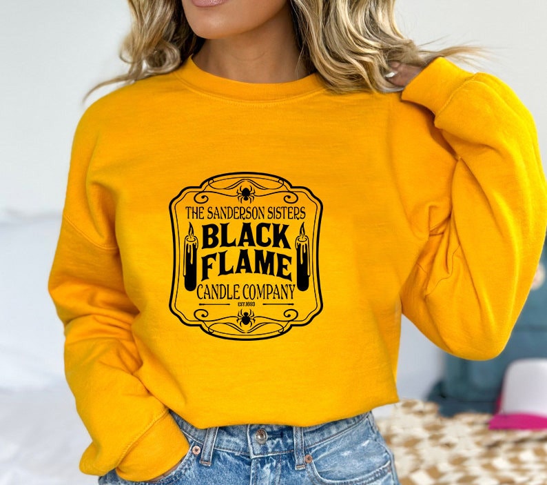 May include: Yellow sweatshirt with a black graphic print of a vintage-style label that reads "The Sanderson Sisters Black Flame Candle Company Est. 1693".
