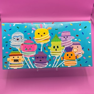 May include: A blue canvas painting with a whimsical design of colorful characters on sticks. The characters are all different shapes and sizes and have unique facial expressions. The background is a light blue with white and colorful confetti.