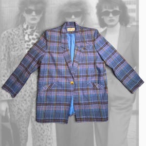 May include: A blue and purple plaid blazer featuring a single gold-tone button closure, notched lapels, long sleeves, and a bright blue interior lining. The garment has a structured fit with a visible brand label at the inner neckline.