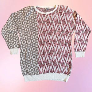 May include: A long-sleeve knit sweater featuring a split-panel design. The left side displays a brown and white geometric triangle pattern, while the right side and sleeves feature a pink and white chevron pattern. It has a white crew neckline.