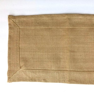 May include: A brown rectangular table runner with a woven texture and a stitched border.