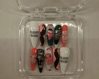 May include: A set of ten long, pointed false nails in a clear plastic case. The nails feature various designs, including photos, a black moustache, and the text "SLUSHY 1000'S". Colours include white, pink, black, and orange.