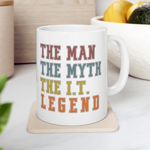May include: White ceramic mug with the text "THE MAN THE MYTH THE I.T. LEGEND" in a retro font with colorful letters. The text is stacked vertically.