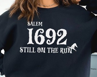 May include: Black sweatshirt with white text that reads "Salem 1692 Still on the Run" with a witch's hat graphic.