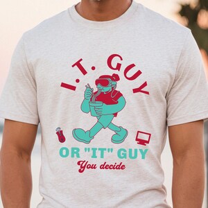 May include: A light gray t-shirt with a cartoon graphic of a person wearing goggles and eating noodles. The text reads "I.T. GUY OR "IT" GUY You decide" in red and teal. A computer mouse and monitor are also featured.