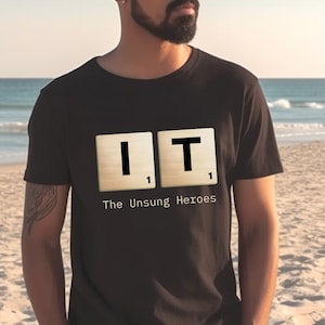 May include: Black t-shirt with a graphic of two Scrabble tiles spelling "IT" with the number "1" on each tile. The text "The Unsung Heroes" is printed below the tiles.