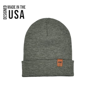 May include: A green waffle knit beanie with a brown leather patch that says "HHI" in black lettering. The beanie is made in the USA.