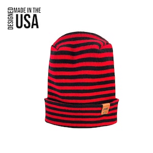 May include: Red and black striped knit beanie with a small brown leather patch that says "MADE" on it. The beanie is made in the USA.
