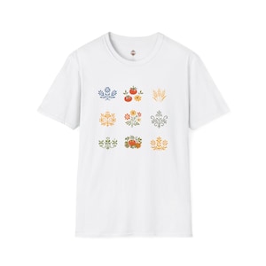 May include: White t-shirt featuring nine colorful floral and botanical designs. The designs include images of tomatoes, wheat, and various flowers in shades of red, yellow, blue, and green. The shirt has a crew neck and short sleeves.