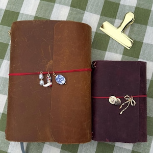 Caderno de viagem recarregável com capa personalizada em couro, feita à mão, com detalhes em relevo e pingentes.