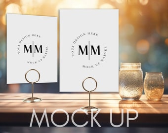 May include: Two white cards with a gold ring holder on a wooden table. The cards have a black circle with the text "YOUR DESIGN HERE" and "MM" in the center. The text "MOCK UP MARVEL" is below the circle.