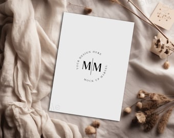 May include: A white card with a circle logo that says "Your Design Here" and "Mock Up Marvel" with the letters "M/M" in the center. The card is on a beige fabric background with dried flowers and a small box with cotton.