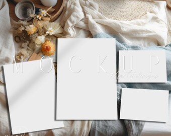May include: Mockup of three blank white cards on a light blue and beige fabric background. The cards are arranged in a staggered formation. The text "MOCKUP" is written in white on the cards. The text "Marvel Designs" is written in white on the bottom card.