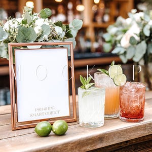 May include: A rose gold framed sign with the text "MOCKUP" and "PSD & JPG SMART OBJECT" sits on a wooden surface. Three cocktails with lime and mint garnishes are in front of the sign. Two green limes are in the foreground.