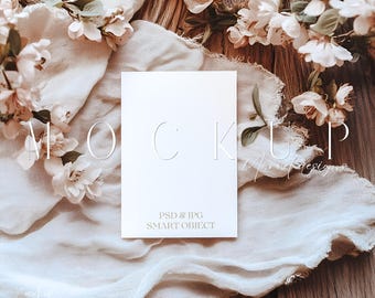 May include: A white card mockup with the text "PSD & JPG SMART OBJECT" on a wooden surface with a white fabric and white flowers.